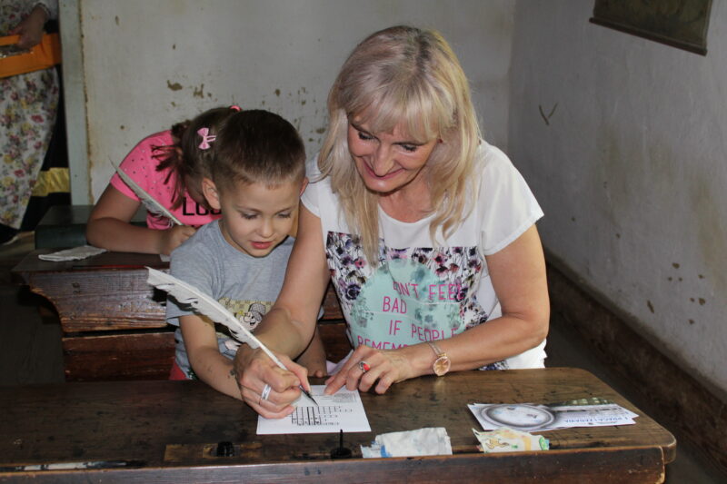 Na zdjęciu babcia i wnuk doskonalą naukę pisania gęsim piórem.