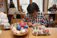 Twórczyni Dorota Kokot ozdabia nożykiem kroszonkę (jajko). Na stole stoi koszyk i opakowanie tekturowe z kroszonkami