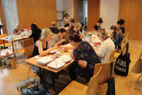 Warsztaty malowania porcelany - grupa uczestniczek dekoruje naczynia przy stole.