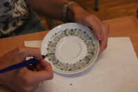 Okrągły spodek porcelanowy - wypełnienie stalówką wzoru kwiatowego w kolorze zielonym.