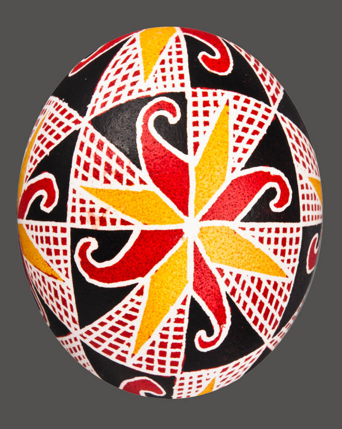 Jajko -pisanka z motywem rozety (w kolorach białym, żółtym i czerwonym) dookoła inne ornamenty geometryczne, tło czarne