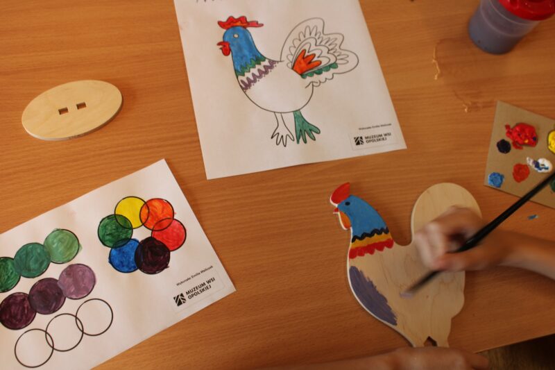 Uczestnik warsztatów maluje ptaka w motywy ludowe na przykładzie wcześniej przygotowanego wzornika.